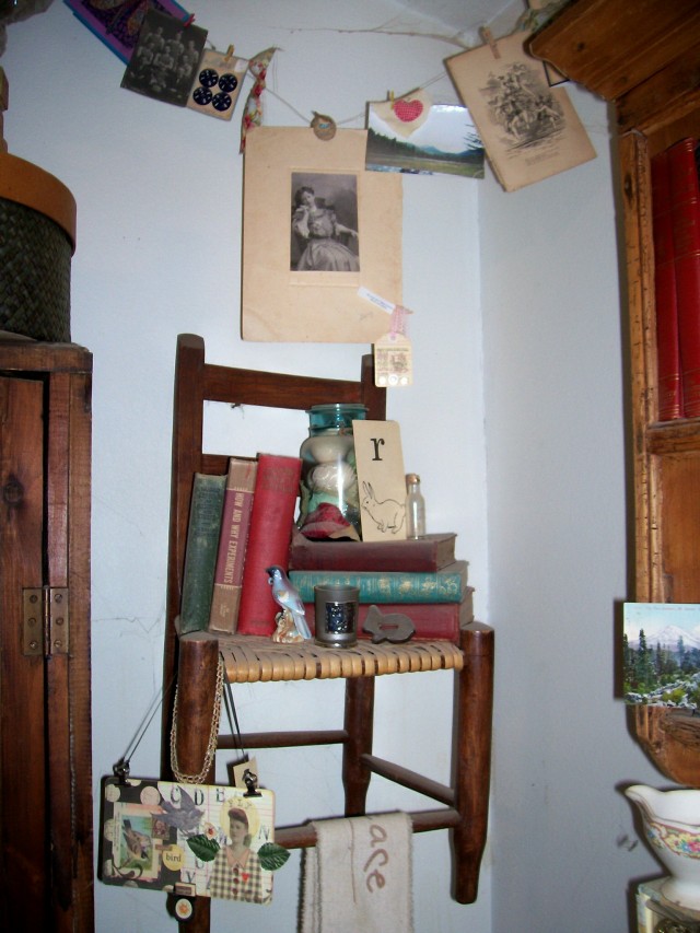 A corner area where I hung a little vintage chair that was my parent's, then topped it with vintage books and bird and rabbit items. A mixed media piece by another artist hangs off the corner and a muslin banner I made with "peace' and decorative stamps hangs over one of the rungs. I've stretched a wire across the corner and hung items from it that I love (including a handmade card from my sister, a photo I took when we lived in WA state and some vintage items etc)